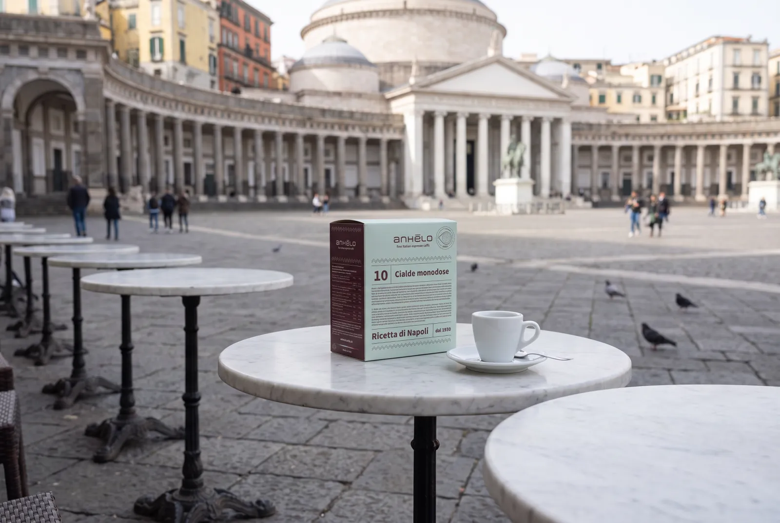Anhelo single-serve pods pack and espresso cup on a marble table in a square in Naples