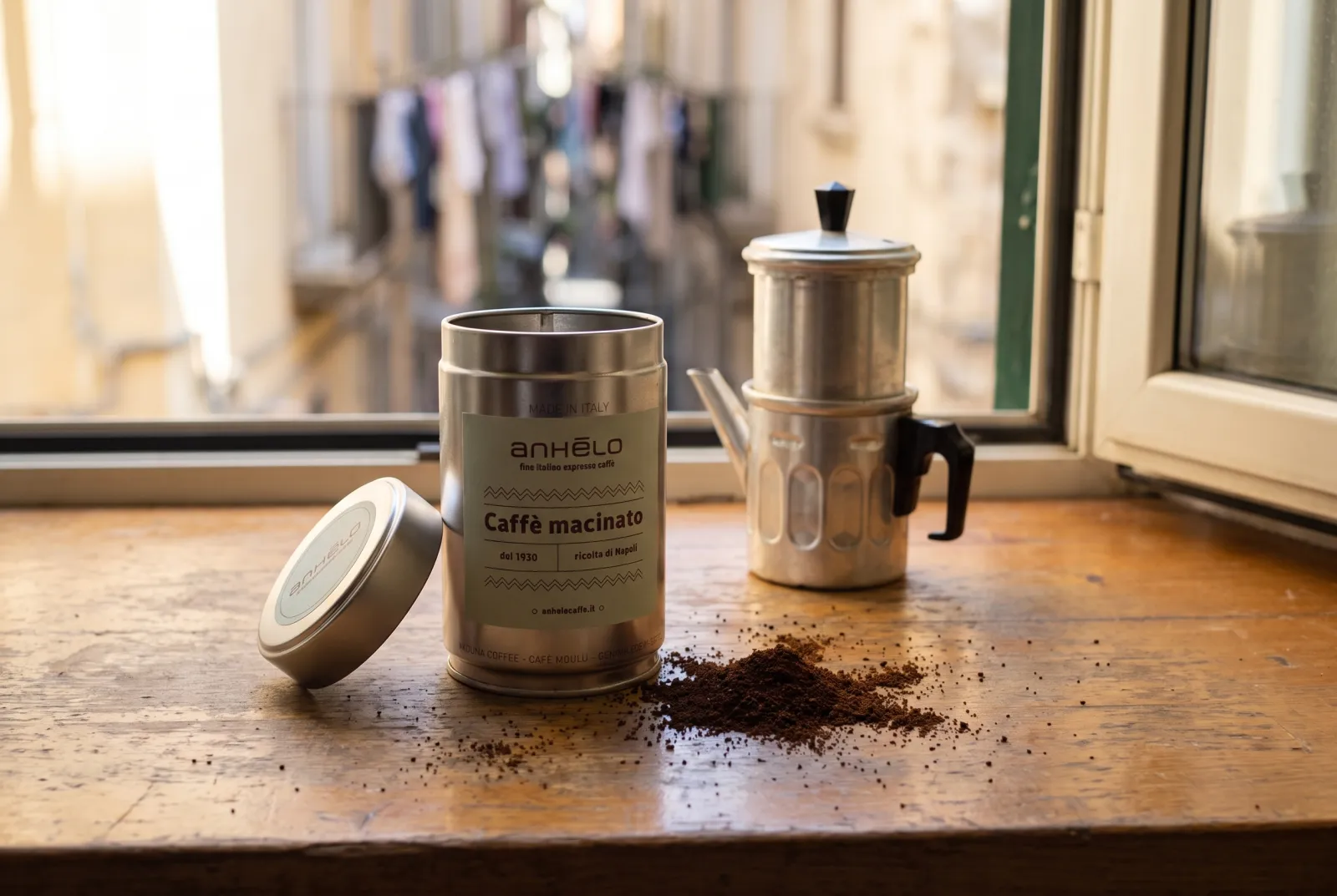 Anhelo ground coffee tin next to a Neapolitan flip coffee pot and a little coffee powder on a windowsill